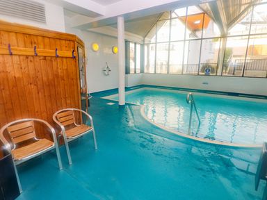 An indoor swimming pool with two chairs and a wooden changing area at Apartment 7 Mansion House in Tenby