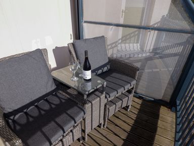 A balcony with two wicker chairs a glass table a bottle of wine and two wine glasses at Apartment 7 Mansion House in Tenby