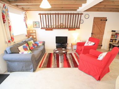 A living room with a gray sofa, red armchairs, a small round table, and a TV at Y Beudy The Old Byre in Llanbedr