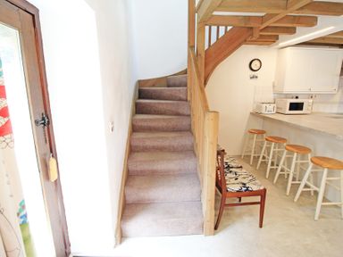 A staircase next to a kitchen counter with stools and a chair with patterned cushions at Y Beudy The Old Byre in Llanbedr