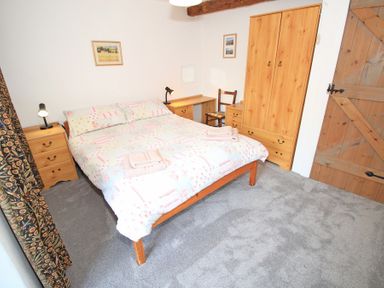 A bedroom with a double bed desk wardrobe bedside tables and a wooden door at Y Beudy The Old Byre in Llanbedr