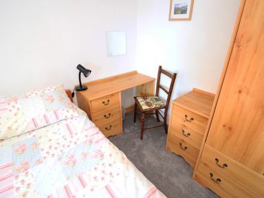 A bedroom with a bed with floral bedding a desk with a lamp a wooden chair a chest of drawers and a wardrobe at Y Beudy The Old Byre in Llanbedr