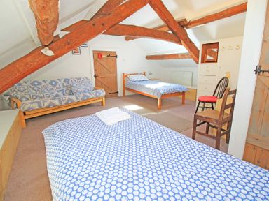 A bedroom with two single beds a sofa two wooden chairs and exposed wooden beams at Y Beudy The Old Byre in Llanbedr