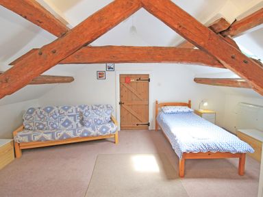 A bedroom with wooden beams a single bed a cushioned sofa and wooden door at Y Beudy The Old Byre in Llanbedr