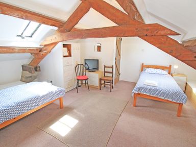 A bedroom with two single beds a television and wooden ceiling beams at Y Beudy The Old Byre in Llanbedr