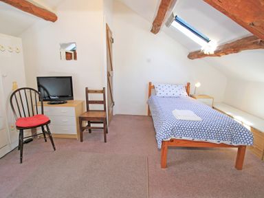 A bedroom with a single bed a dresser with a television two chairs and exposed wooden beams at Y Beudy The Old Byre in Llanbedr