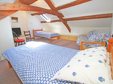 A bedroom with two single beds a wooden sofa a small TV on a stand and exposed wooden ceiling beams at Y Beudy The Old Byre in Llanbedr