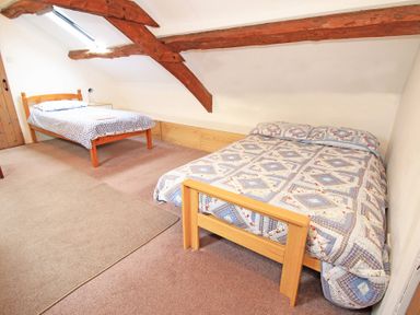 A bedroom with two wooden beds and exposed ceiling beams at Y Beudy The Old Byre in Llanbedr