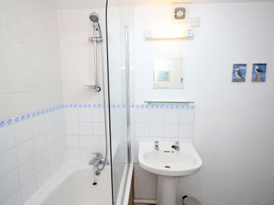 A bathroom with a bathtub and shower next to a sink with a mirror above at Y Beudy The Old Byre in Llanbedr