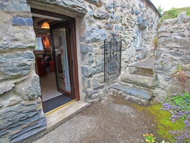 A stone building entrance with an open door leading inside and stone steps next to it at Y Beudy The Old Byre in Llanbedr