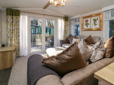 A living room with brown sofas pillows floral curtains and glass doors opening to an outdoor deck at Lily Rose Lodge White Cross Bay near Troutbeck Bridge