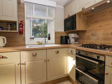 A kitchen with cream cabinets wooden countertops a window with white blinds a gas stove an oven a microwave a coffee machine and a kettle at Lily Rose Lodge White Cross Bay near Troutbeck Bridge
