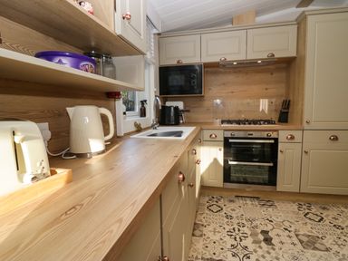 A kitchen with wooden countertops beige cabinets a toaster kettle microwave oven stovetop and patterned floor at Lily Rose Lodge White Cross Bay near Troutbeck Bridge