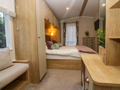 A bedroom with a bed cushions a dresser a window with curtains and a built in wardrobe at Lily Rose Lodge in White Cross Bay near Troutbeck Bridge