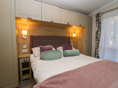 A bedroom with a double bed with pillows and bolsters built in cabinets and wall lamps at Lily Rose Lodge White Cross Bay near Troutbeck Bridge