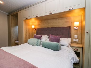 A bedroom with a bed with pillows and cushions under built in cabinets with lights at Lily Rose Lodge in White Cross Bay near Troutbeck Bridge