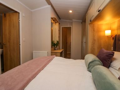 A bedroom with a bed with cushions bedside lamp wardrobe and vanity desk at Lily Rose Lodge White Cross Bay near Troutbeck Bridge