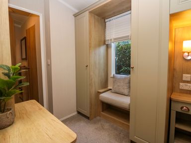 A small room with a built-in window seat between two wardrobes and a desk with a plant on it at Lily Rose Lodge in White Cross Bay near Troutbeck Bridge