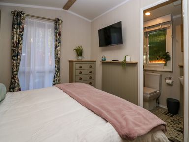 A bedroom with a bed a chest of drawers a wall-mounted television and an en suite bathroom at Lily Rose Lodge in White Cross Bay near Troutbeck Bridge