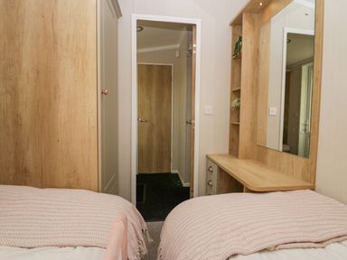 A bedroom with two beds a wooden wardrobe a dressing table with a mirror and a wooden door at Lily Rose Lodge White Cross Bay near Troutbeck Bridge