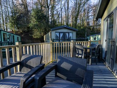 An outdoor deck with black wicker chairs and a table near wooded mobile homes at Lily Rose Lodge White Cross Bay near Troutbeck Bridge