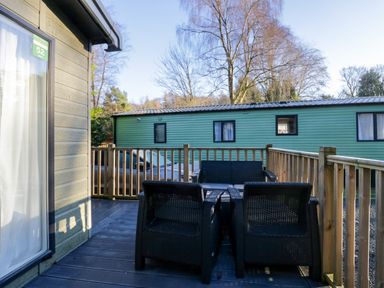 An outdoor deck with black woven chairs and a sofa next to a wooden railing and a green caravan at Lily Rose Lodge White Cross Bay near Troutbeck Bridge