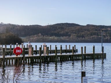 A wooden pier extending into a lake with seagulls perched on posts and hills in the background at Lily Rose Lodge in White Cross Bay near Troutbeck Bridge