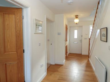 A hallway with wooden floor a white front door wooden interior doors and framed pictures on walls at 4 Centurion Rise in Penrith