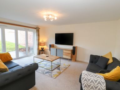 A living room with two dark sofas yellow pillows a wooden coffee table a TV on a wooden sideboard a lamp and sliding glass doors at 4 Centurion Rise in Penrith