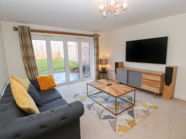 A living room with a gray sofa yellow and gray cushions a wooden coffee table a patterned rug a wooden TV cabinet a wall-mounted TV and sliding glass doors at 4 Centurion Rise in Penrith