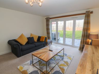 A living room with a dark sofa with yellow cushions a wooden coffee table on a patterned rug sliding glass doors with plaid curtains and a wooden sideboard at 4 Centurion Rise in Penrith