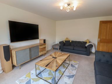 A living room with a wall-mounted television a wooden cabinet two dark sofas a wooden coffee table and a rug with a bird pattern at 4 Centurion Rise Penrith