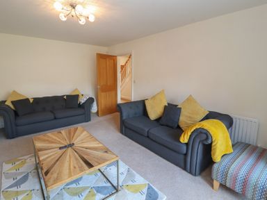 A living room with two dark sofas yellow and black cushions a wooden coffee table and patterned footstool at 4 Centurion Rise in Penrith