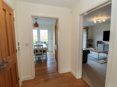 A hallway with wooden floor leading to a dining room with a table and chairs and a living room with a coffee table and television at 4 Centurion Rise Penrith