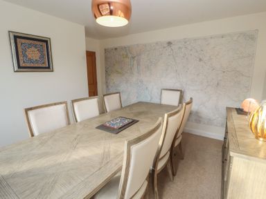 A dining room with eight chairs around a wooden table a large map on the wall and a sideboard with decorative items at 4 Centurion Rise in Penrith