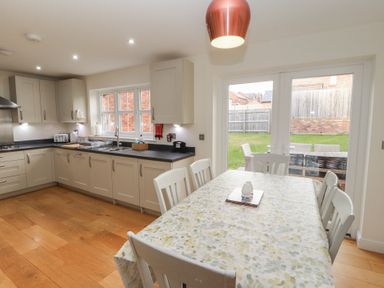 A kitchen with cabinets and a countertop and a dining table with chairs by glass doors at 4 Centurion Rise in Penrith