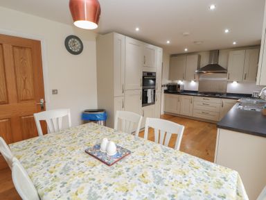 A kitchen with white cabinets a wooden door and a table covered with a patterned tablecloth at 4 Centurion Rise in Penrith