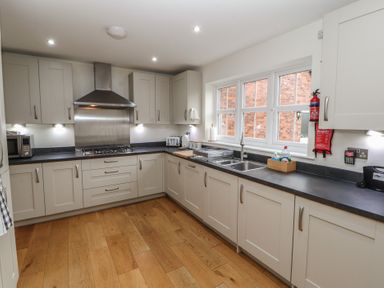 A kitchen with white cabinets black countertops a stainless steel stove under a hood a double sink microwave toaster and wooden floor at 4 Centurion Rise Penrith