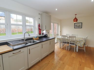 A kitchen with white cabinets a black countertop a stainless steel sink and a dining table with six chairs at 4 Centurion Rise in Penrith