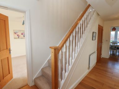 A hallway with a carpeted staircase and wooden handrail beside rooms with wooden doors at 4 Centurion Rise in Penrith