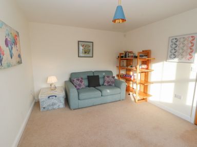 A small living room with a blue sofa and cushions a plastic storage box with a lamp open wooden shelving unit with books and games and wall art at 4 Centurion Rise in Penrith