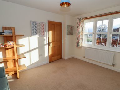 A room with a wooden door a window with floral curtains a wooden shelf with items and a radiator at 4 Centurion Rise in Penrith