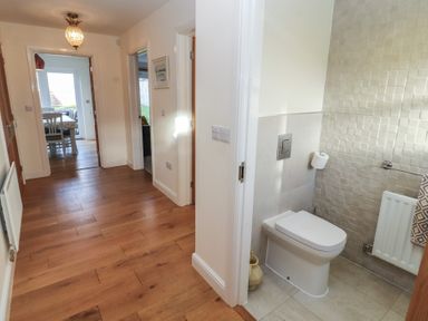 A hallway with wooden floors leading to a dining area and a bathroom with a toilet at 4 Centurion Rise in Penrith