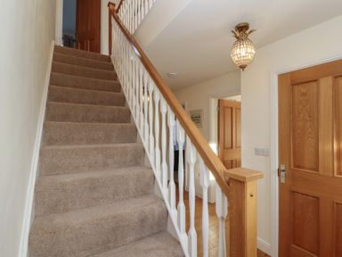 A carpeted staircase with wooden handrails and white balusters next to wooden doors in a hallway at 4 Centurion Rise in Penrith