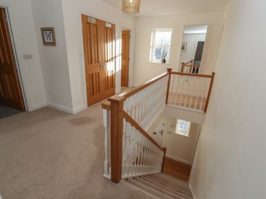 A carpeted stairway with wooden handrails and a hallway with wooden doors and a window at 4 Centurion Rise in Penrith