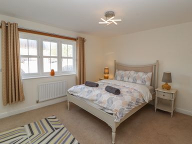 A bedroom with a double bed two bedside tables with lamps a window with curtains and a patterned rug on the floor at 4 Centurion Rise Penrith