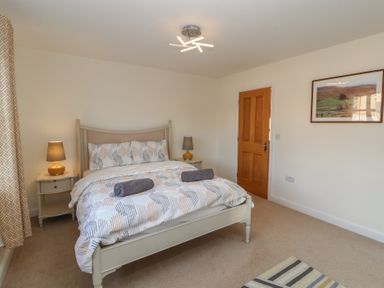 A bedroom with a bed, two bedside tables with lamps, a wooden door, a framed picture on the wall, and striped rug at 4 Centurion Rise in Penrith