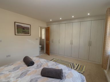 A bedroom with a bed, rolled towels on the bed, built-in wardrobes, a rug, and an open door leading to a bathroom at 4 Centurion Rise Penrith