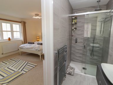 A bedroom with a bed and a patterned rug next to a bathroom with a glass shower at 4 Centurion Rise in Penrith
