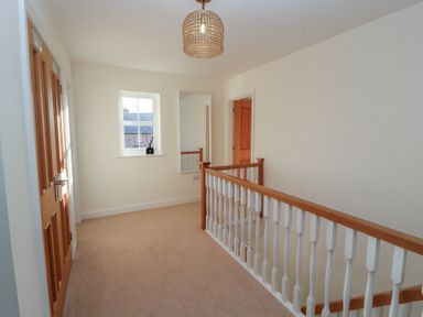 A hallway with beige carpet wooden doors a small window and a railing at 4 Centurion Rise in Penrith